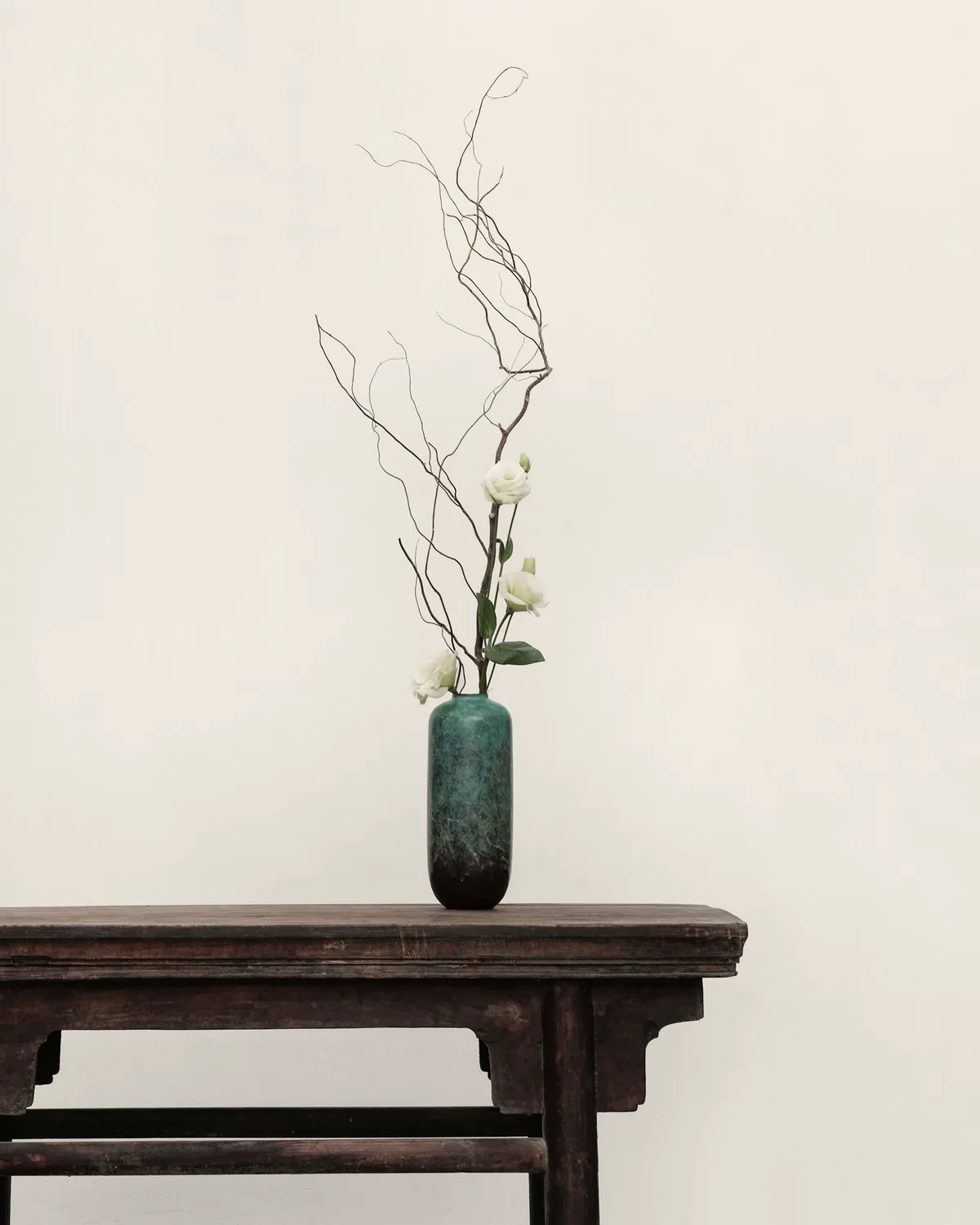 Aged dark-wood console table with a green glazed vase against a pale plaster wall