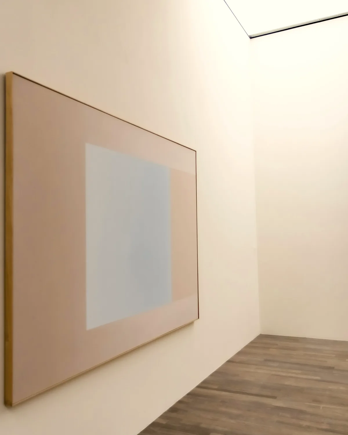 Large framed abstract canvas in pale pink and blue on a gallery wall beneath a skylight