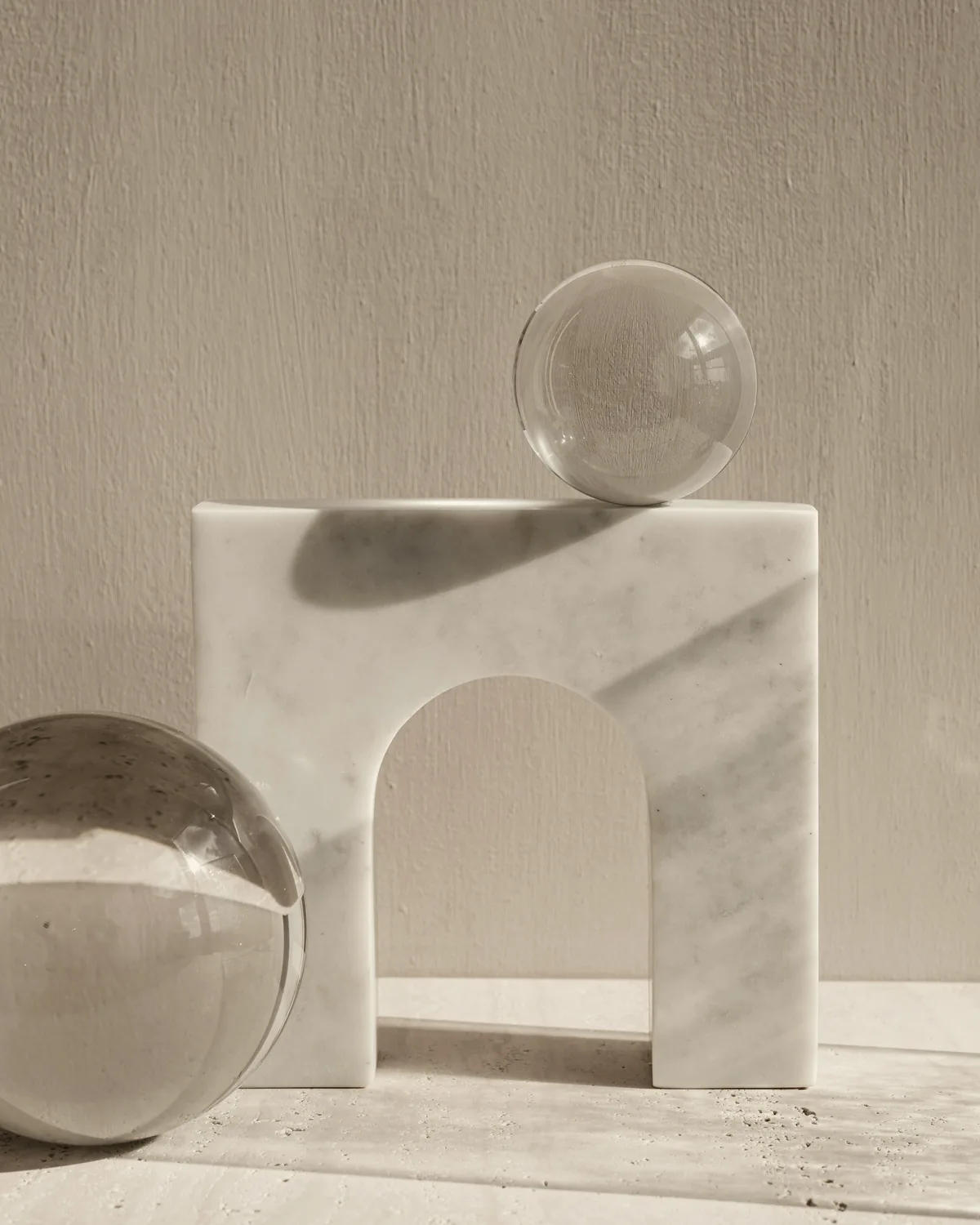 White marble arch with two clear glass spheres against a textured plaster wall