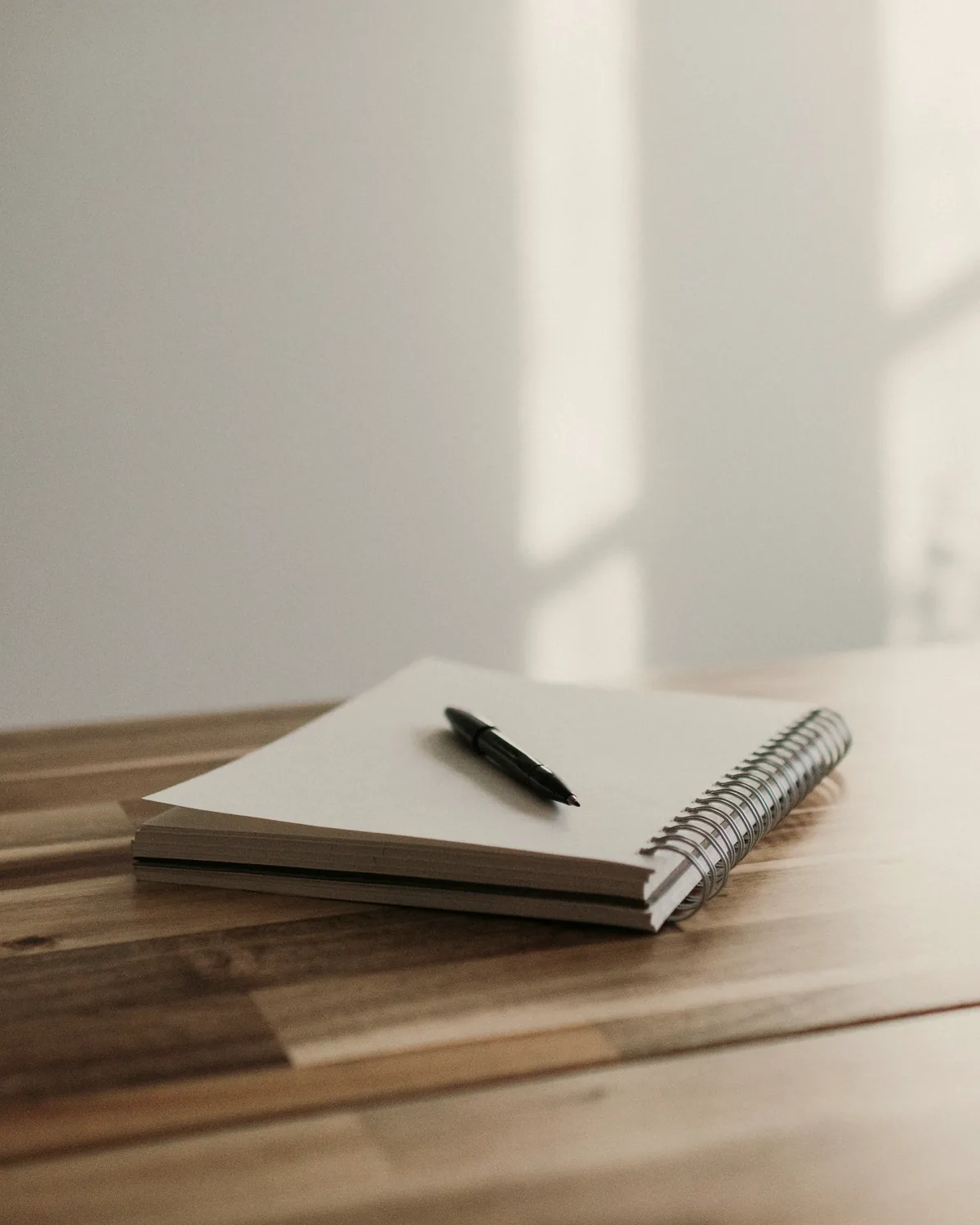 Spiral notebook and a black pen on a wooden desk in soft window light