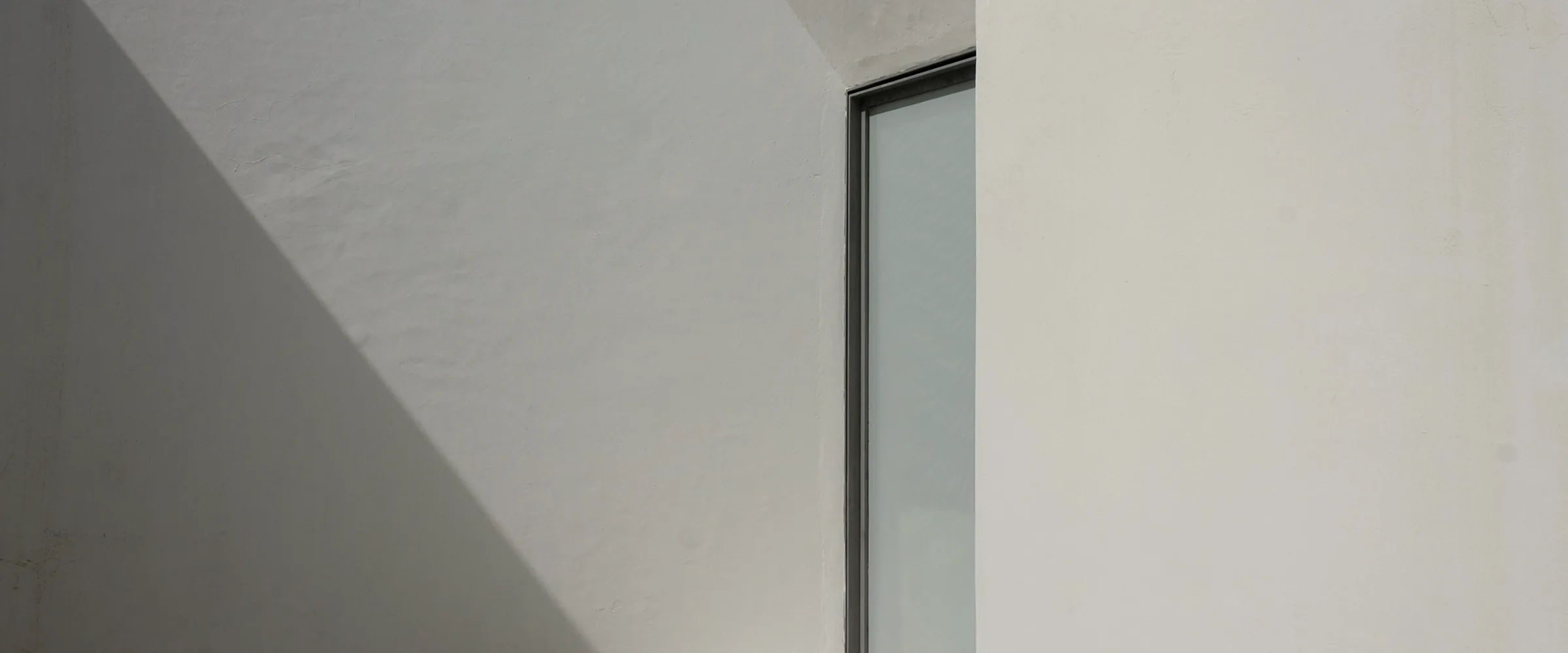 Sunlit white plaster courtyard walls with a tall glass door and a diagonal shadow
