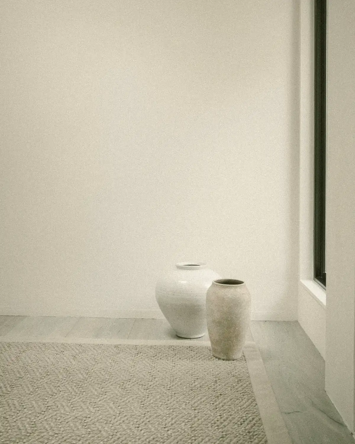 Two ceramic vases on a woven rug in a sunlit white room