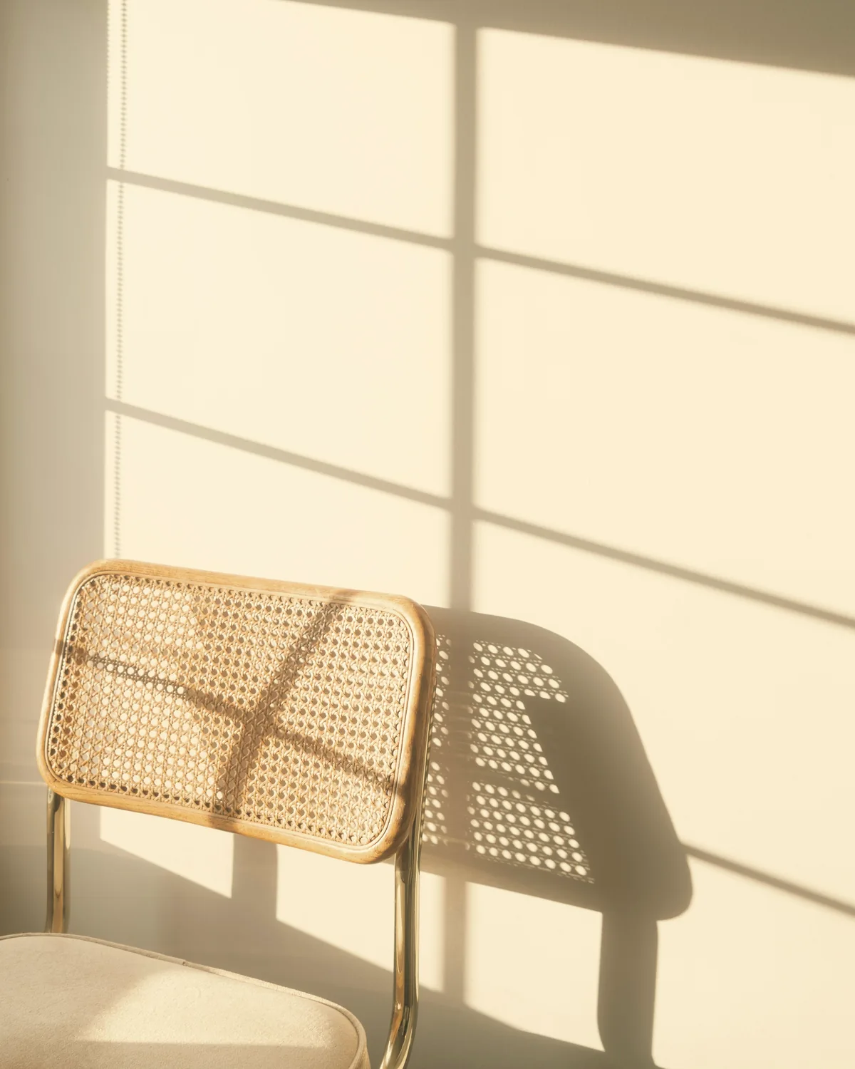 Cane-backed chair in a patch of window light against a cream wall