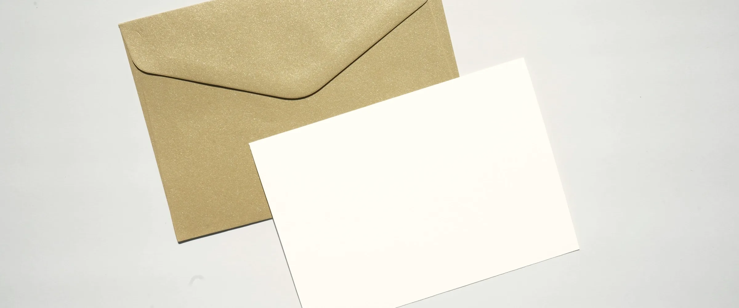 Blank white card resting on a gold envelope against a pale grey surface