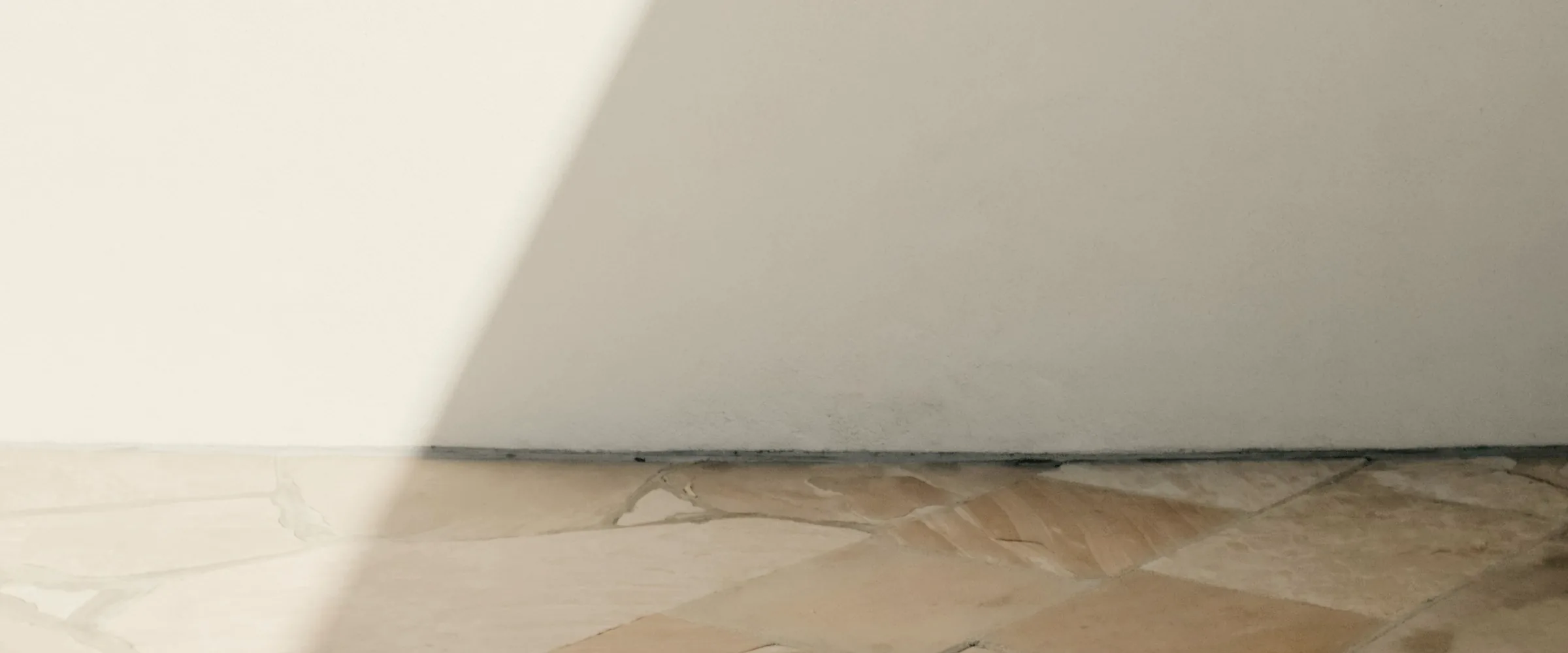 Diagonal sunlight across a white plaster wall above a sandstone floor