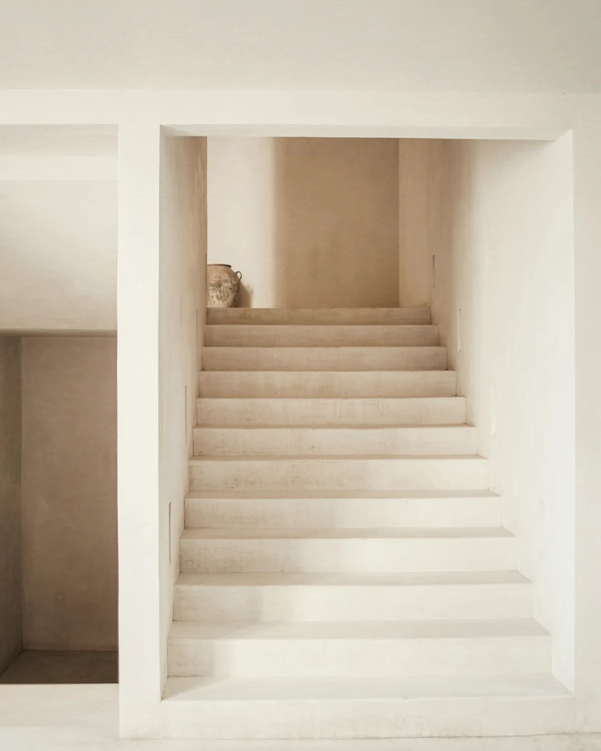 Pale plaster staircase rising to a landing with a single clay vase