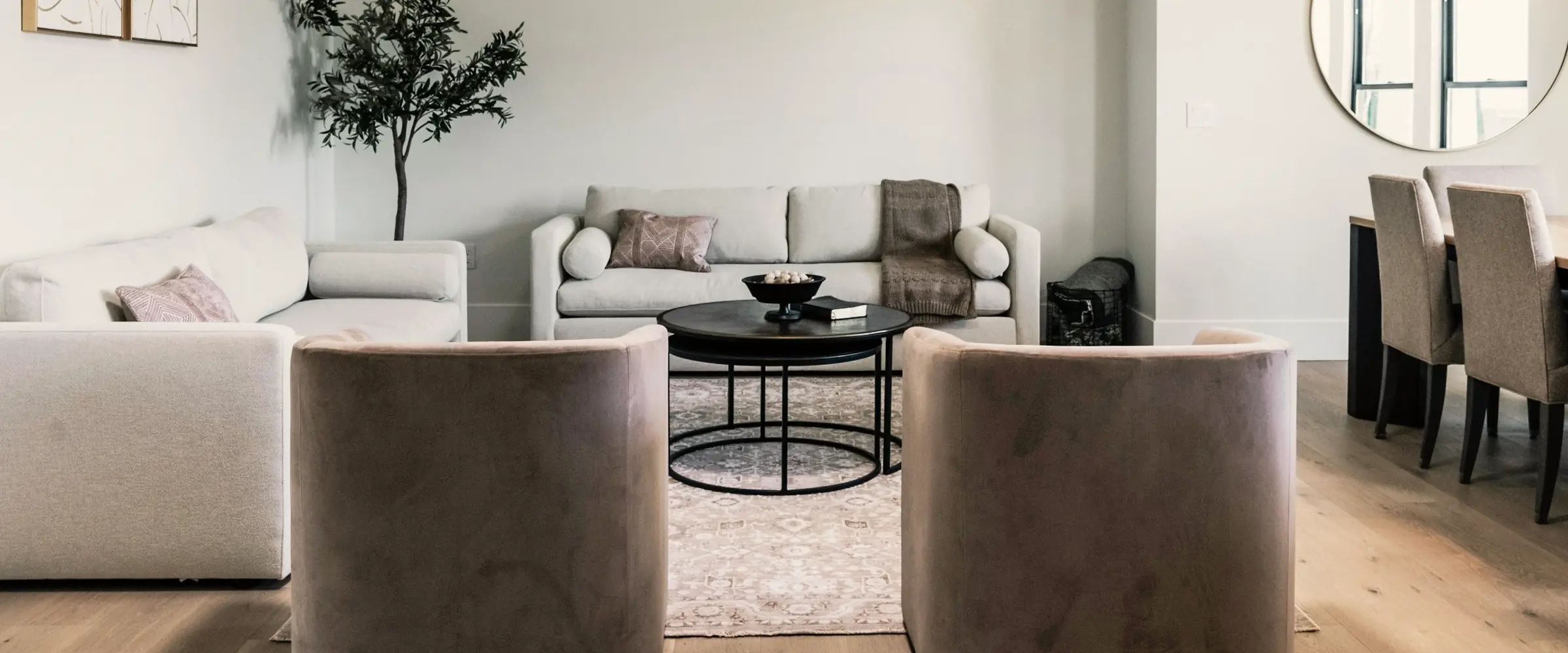 Bright living room with linen sofas, two velvet tub chairs and a round black coffee table on a pale rug