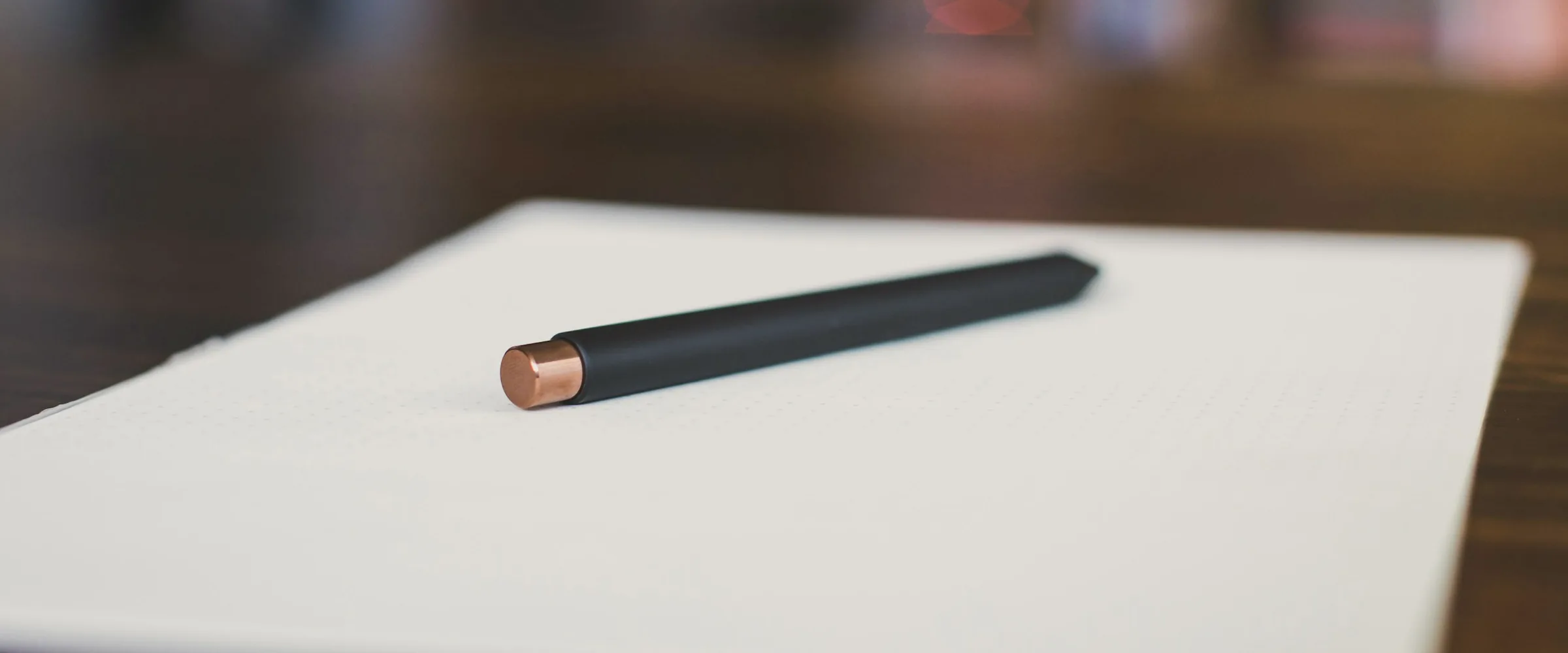A black pen with a copper cap resting on a blank notebook page