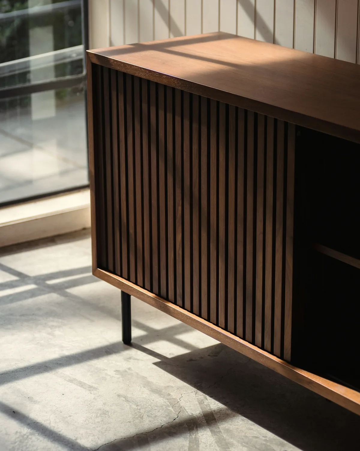 Walnut slatted sideboard on a concrete floor in raking window light