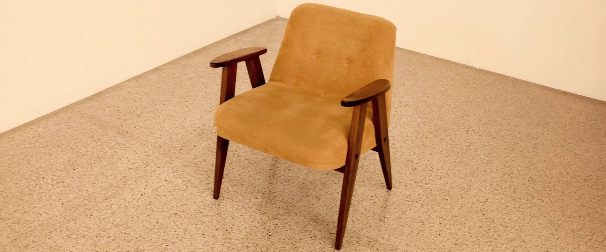Mid-century armchair in mustard upholstery with walnut arms, alone in the corner of a pale room