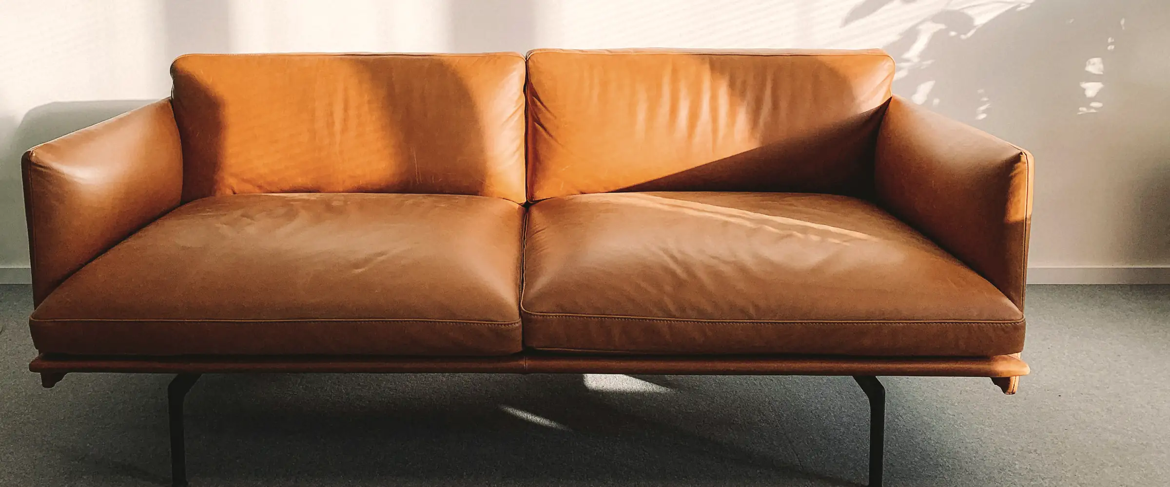 Tan leather two-seat sofa against a sunlit white wall