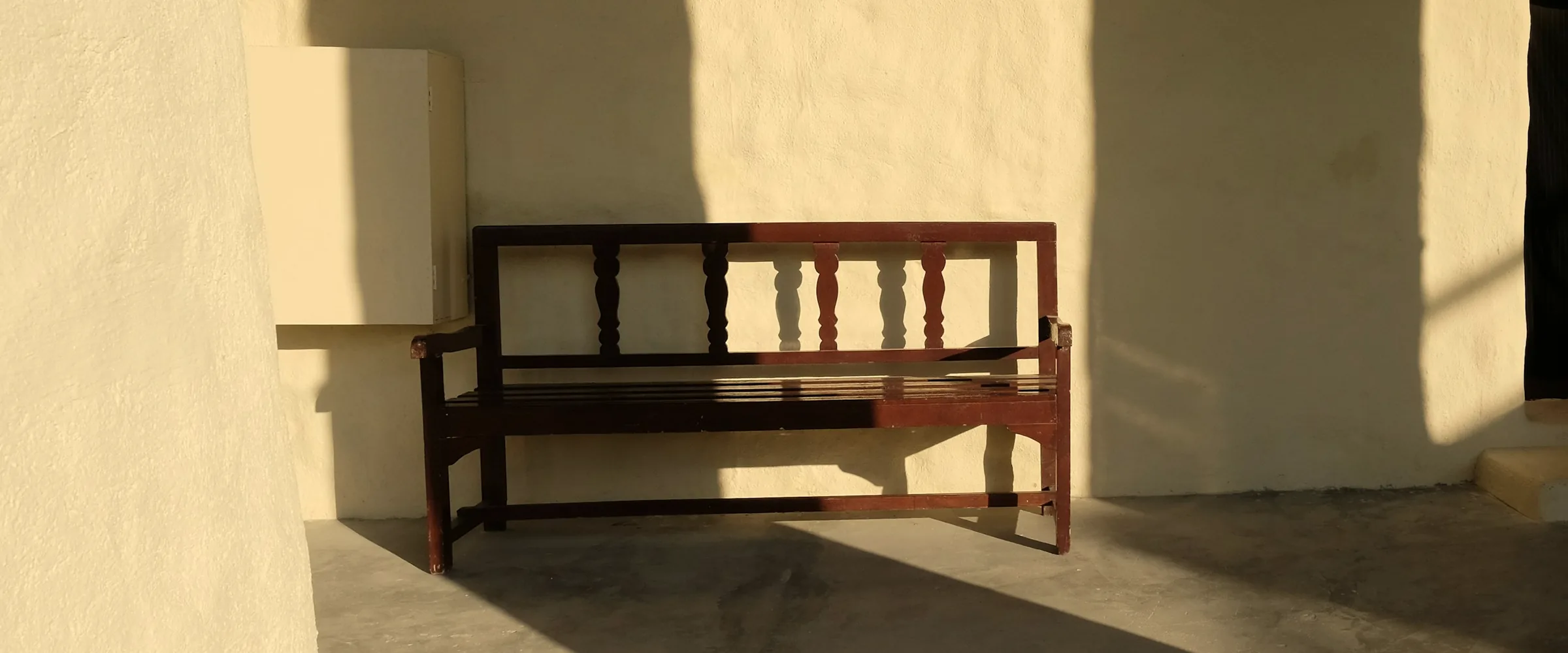 Dark timber bench against a sunlit plaster wall, half in shadow