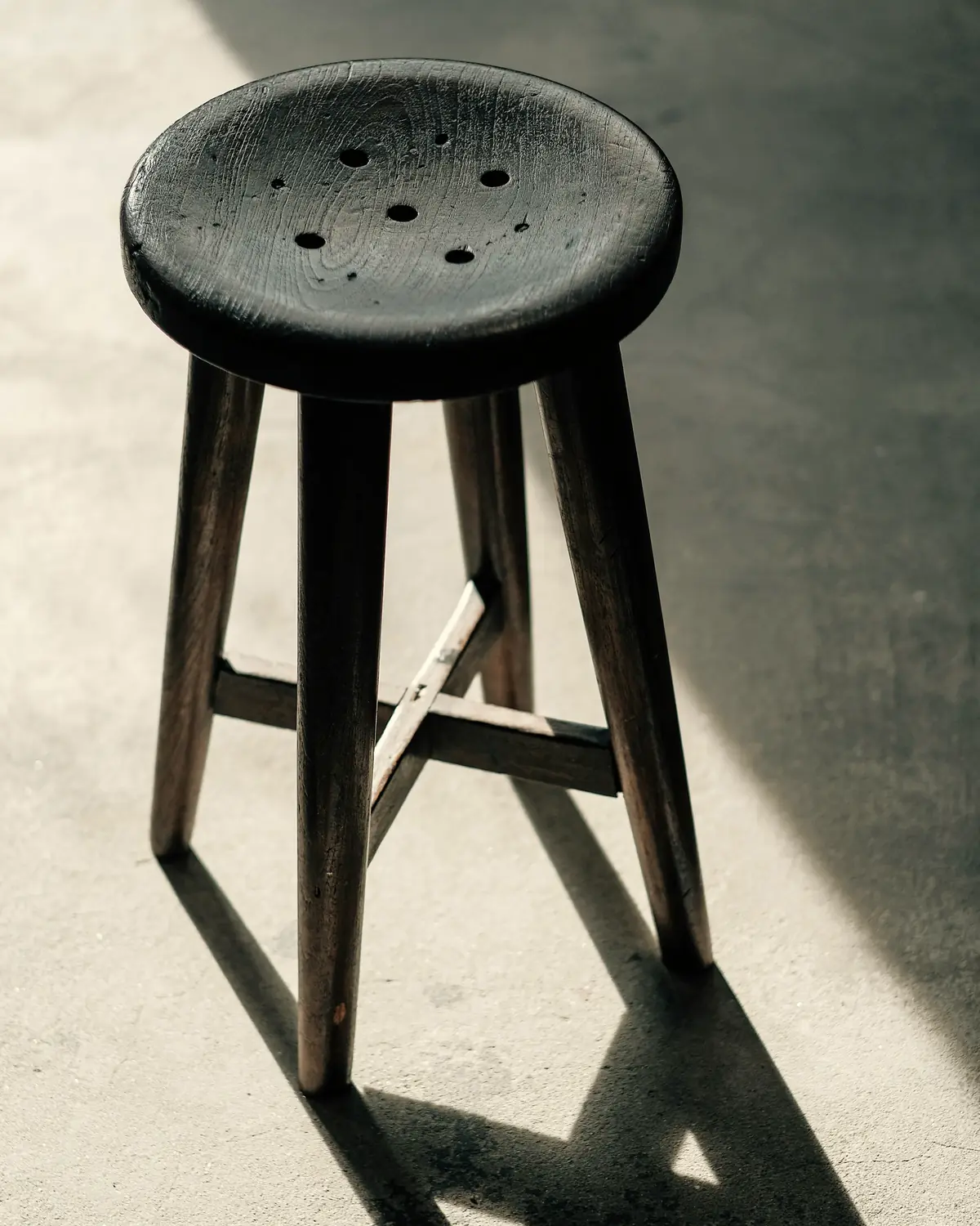 Dark timber stool casting a long shadow across a concrete floor