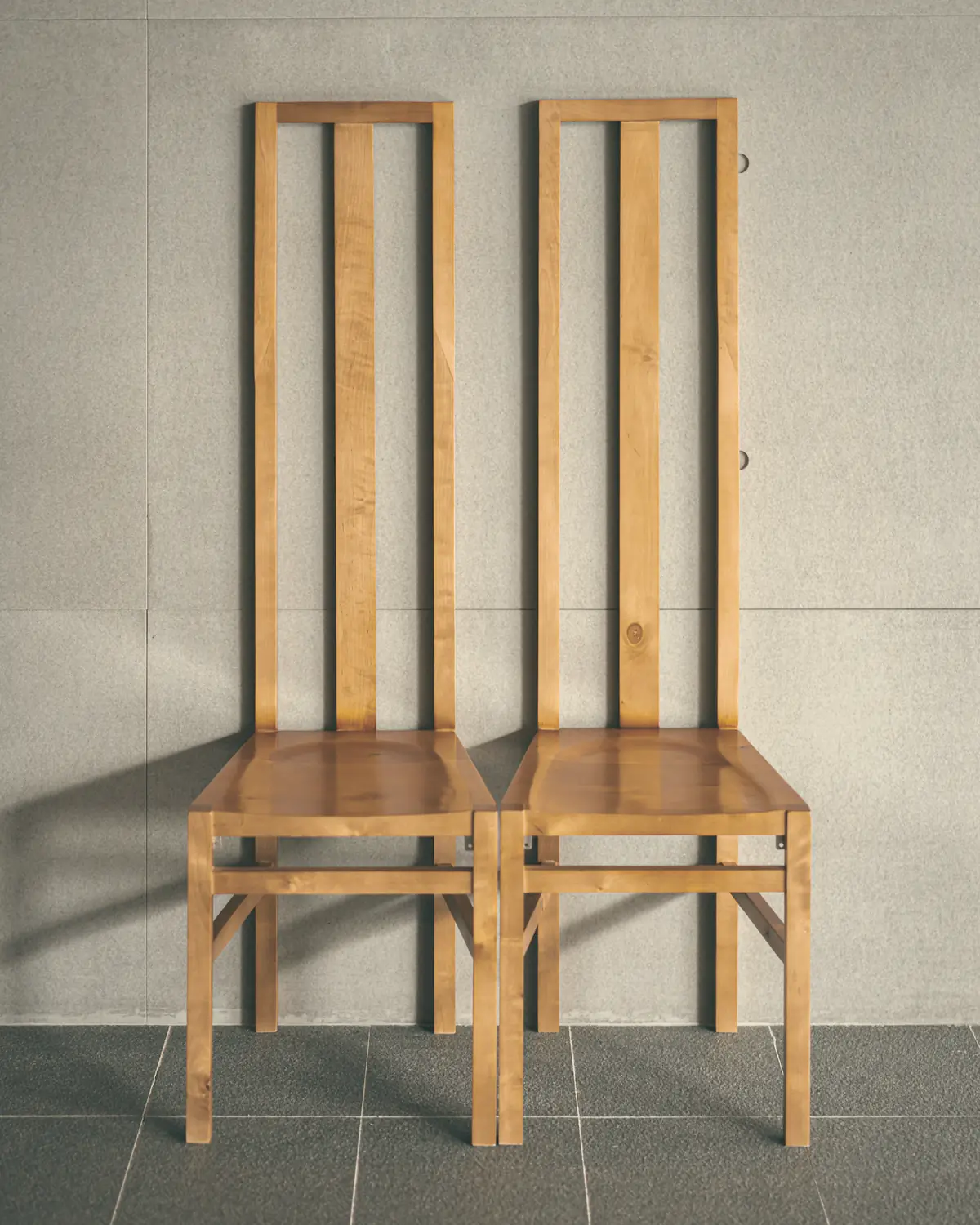 Two high-back solid-wood chairs against a board-formed concrete wall