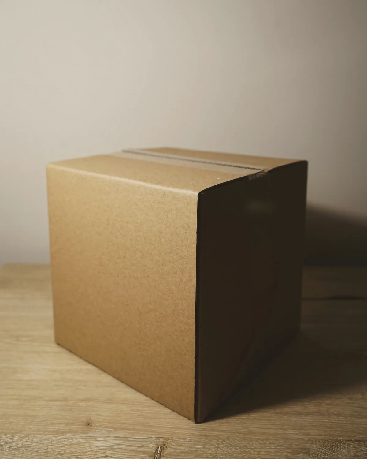 A sealed cardboard carton on a pale wooden surface against a plaster wall
