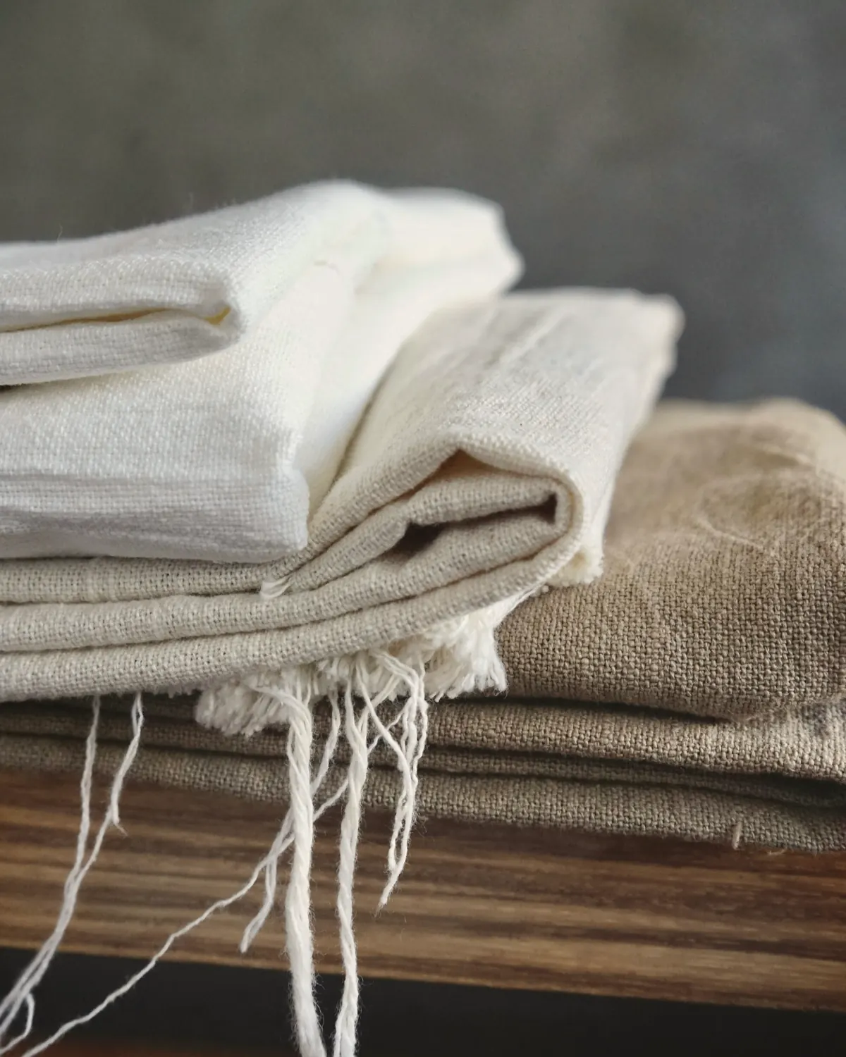 Folded linen and cotton in white and flax tones stacked on a wooden bench