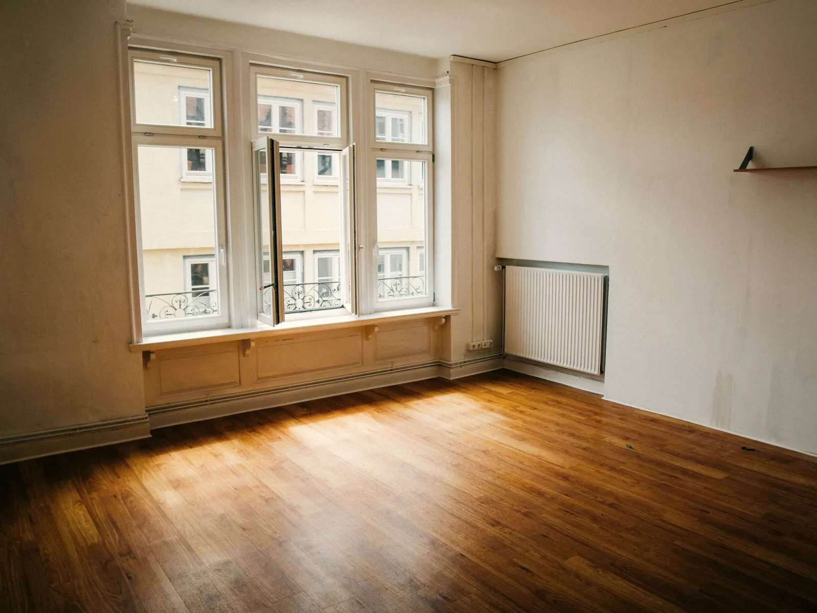 Empty sunlit room with tall windows and a warm wooden floor