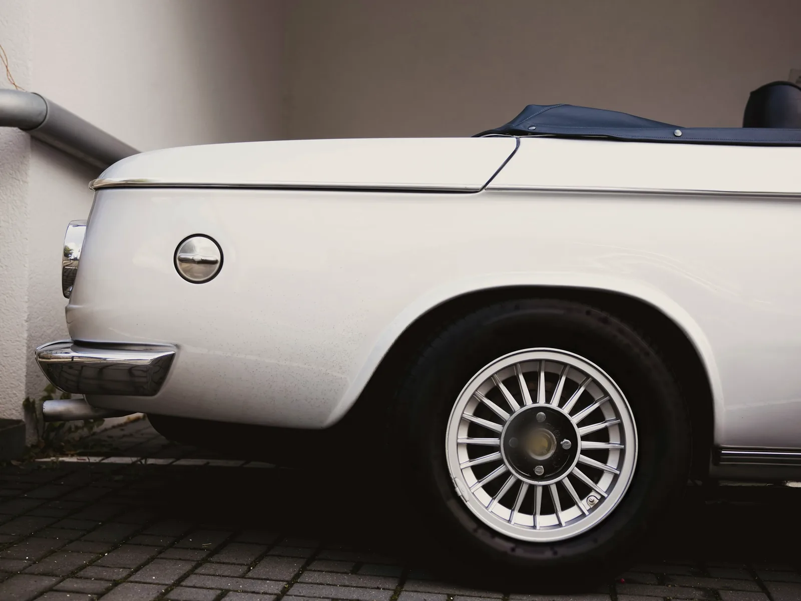 Rear quarter of a white classic convertible parked in a plaster-walled carport