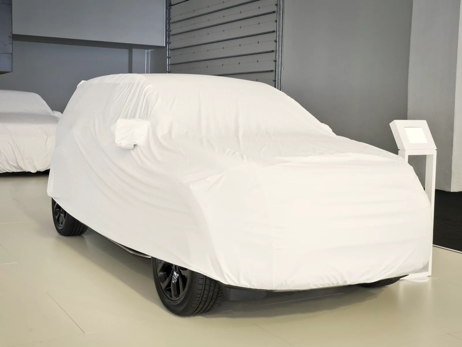 Two cars under fitted white covers in a bright, empty showroom