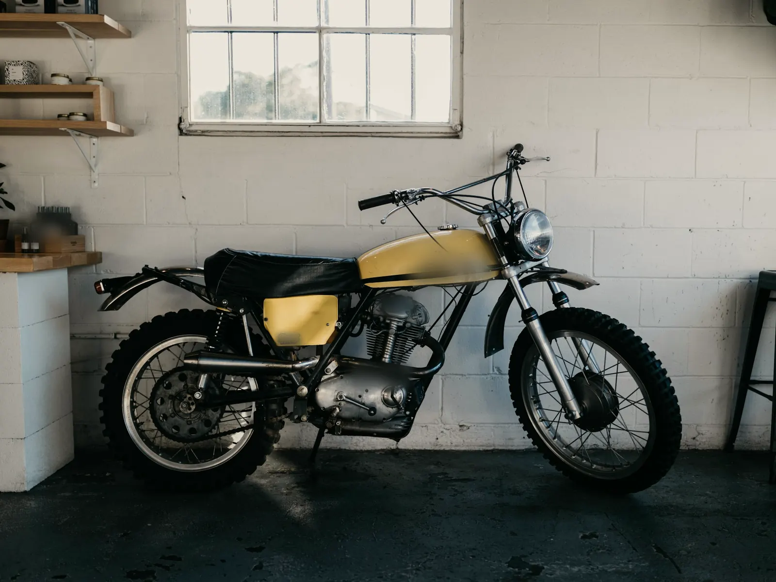 Vintage yellow scrambler motorcycle against a white-painted block wall