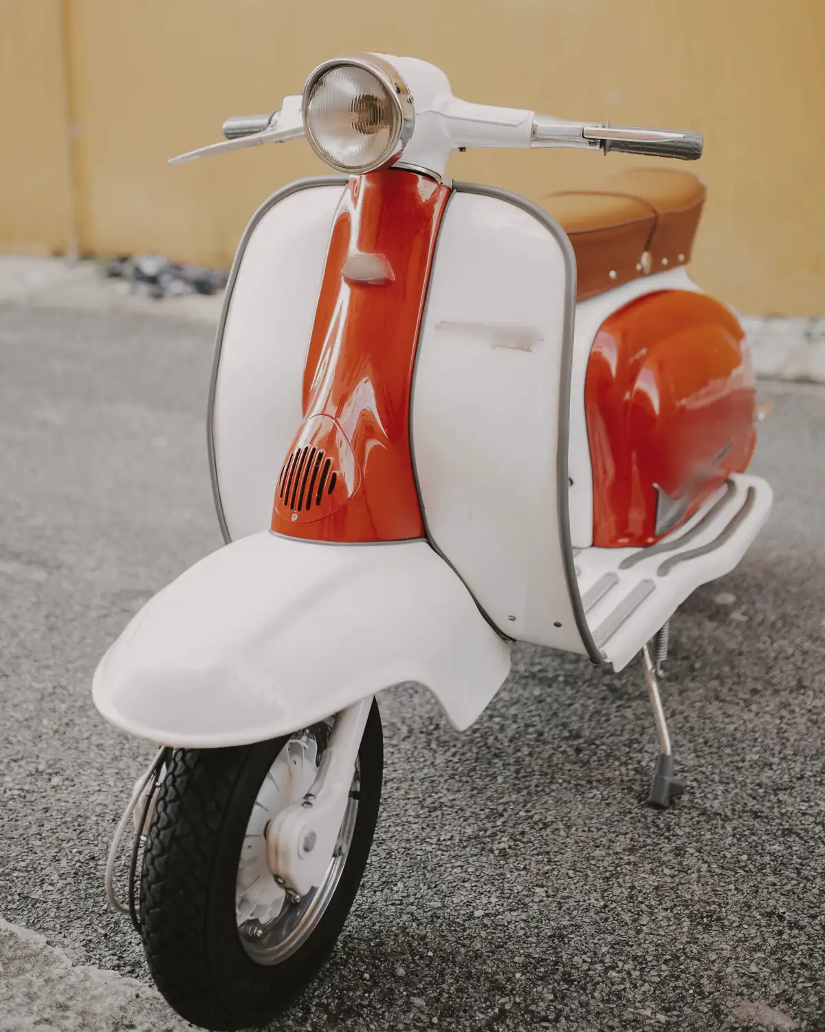 Restored white and orange vintage scooter on asphalt in front of an ochre wall
